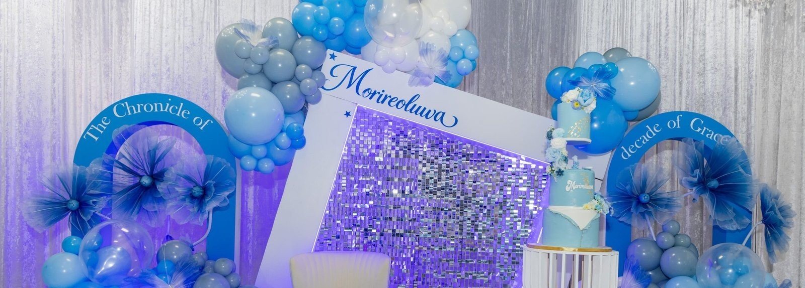 A blue and silver balloon installation with a sequin backdrop and tiered cake set for a milestone celebration at The Hendrix, Stafford