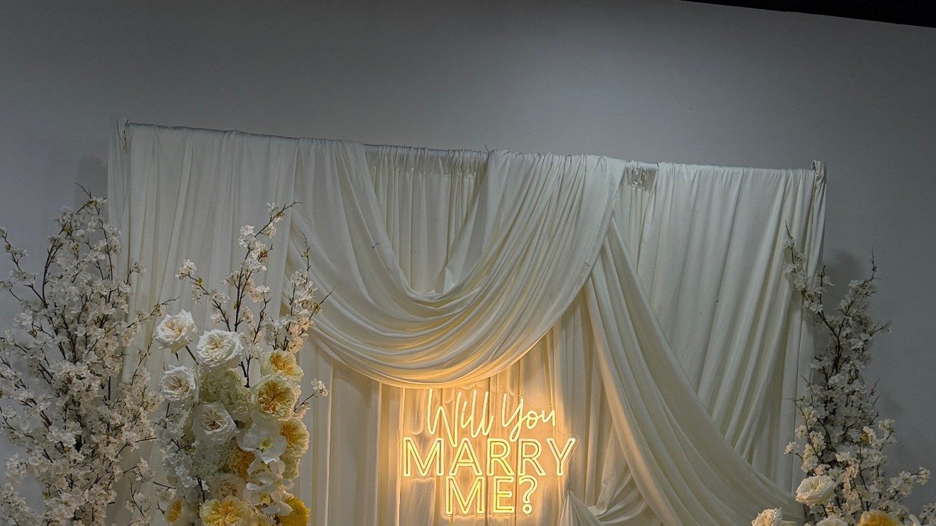 A draped proposal backdrop with a glowing Will You Marry Me neon sign and florals at The Hendrix, Stafford