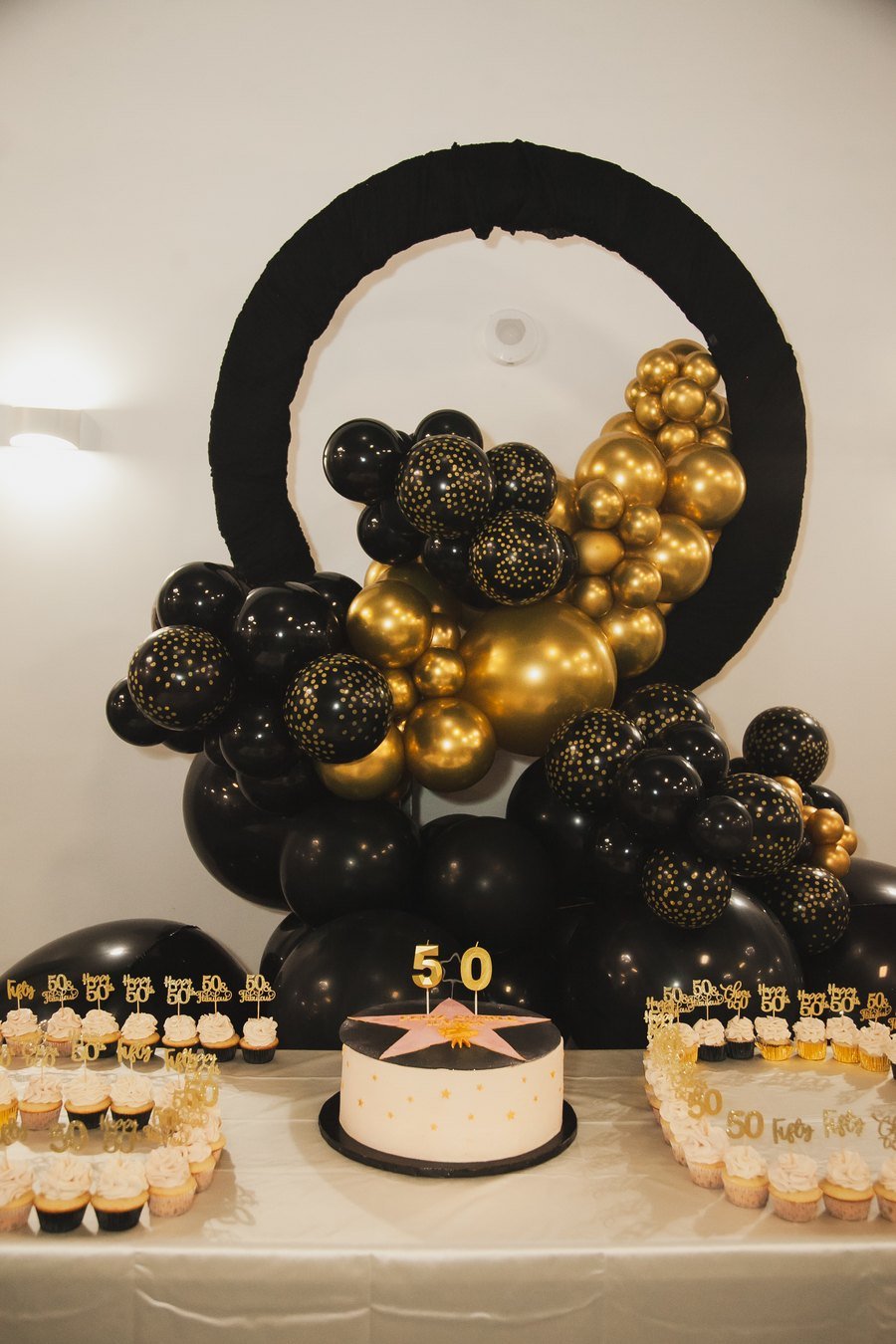 A black balloon hoop over a dessert table of cupcakes and a birthday cake at The Hendrix