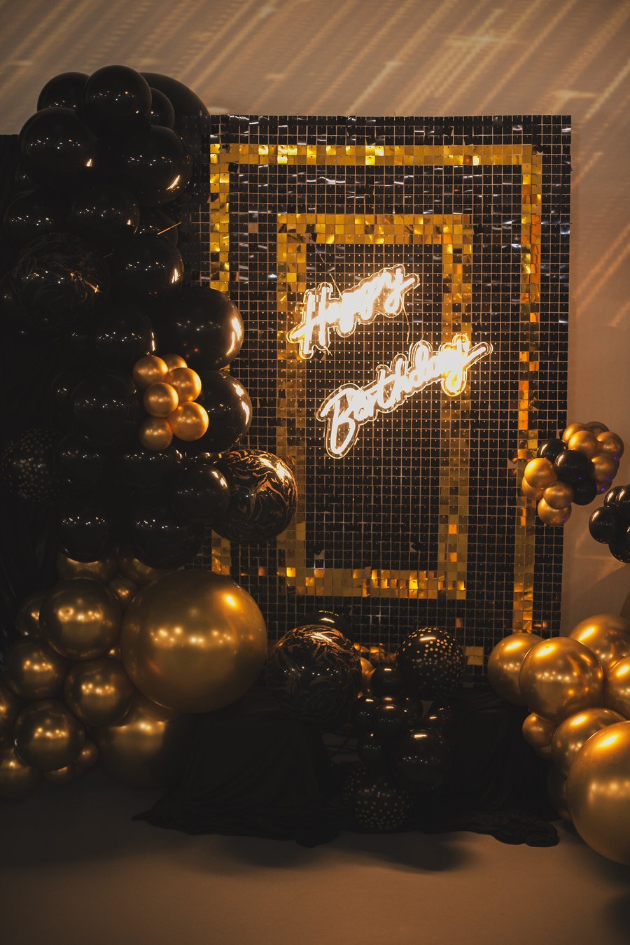 A gold sequin backdrop with a neon Happy Birthday sign and chrome balloons at The Hendrix