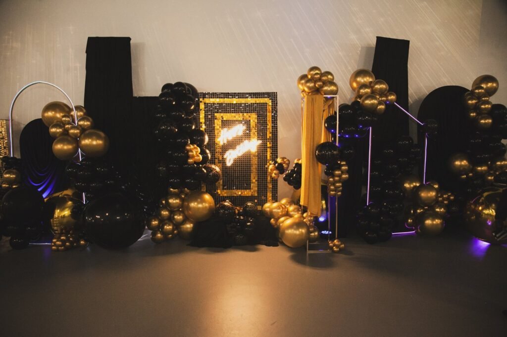 A black and gold sequin photo backdrop with a neon sign and balloon towers at The Hendrix