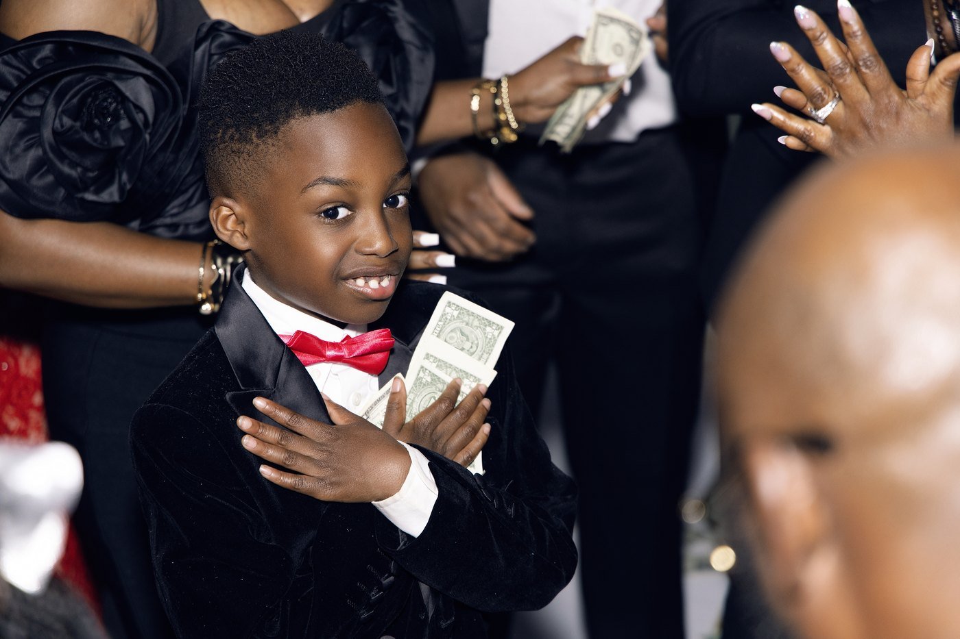 A boy in a tuxedo holding dollar bills during the money spray at a Nigerian party at The Hendrix