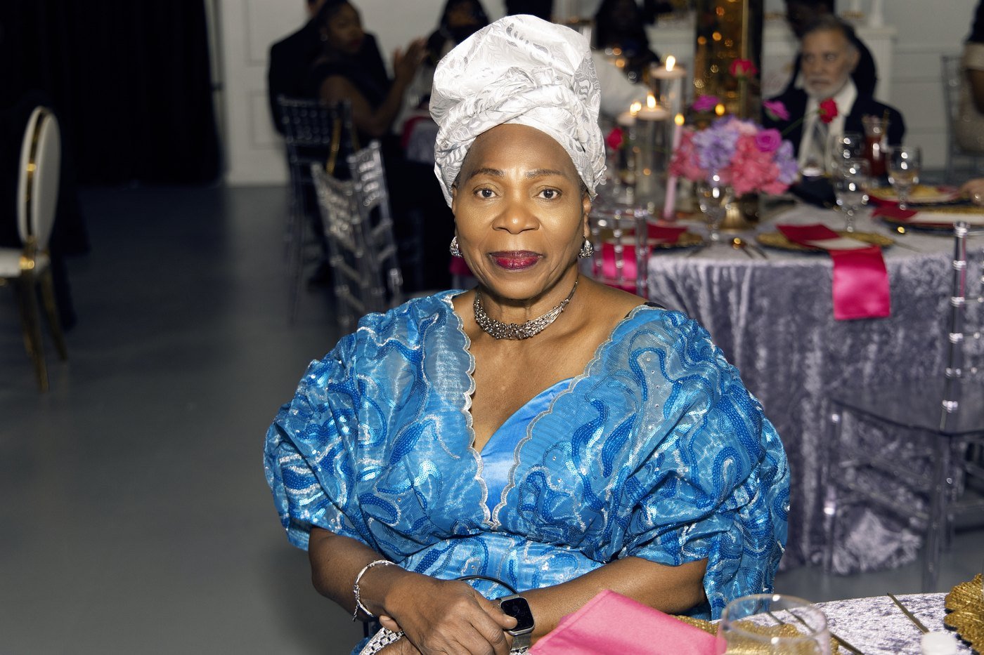 A guest in a blue damask buba and white gele seated at a lilac linen table at The Hendrix