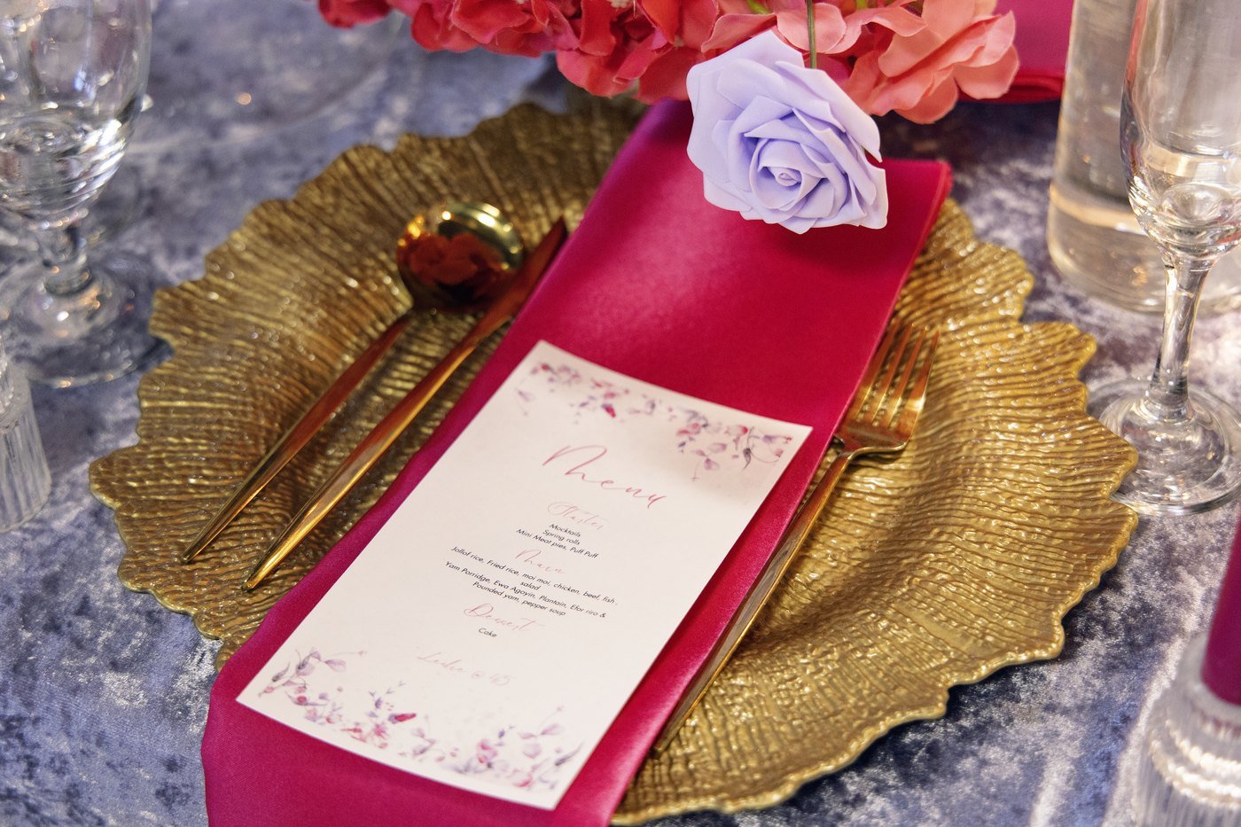 A place setting with a gold scallop charger, fuchsia napkin and printed menu card at The Hendrix