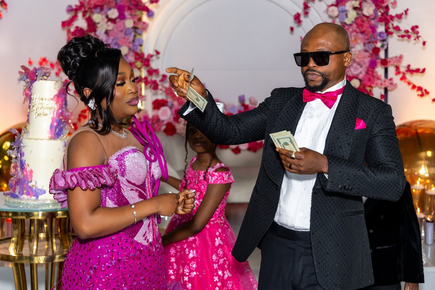 The celebrant's husband spraying notes beside the cake as their daughter looks on at The Hendrix
