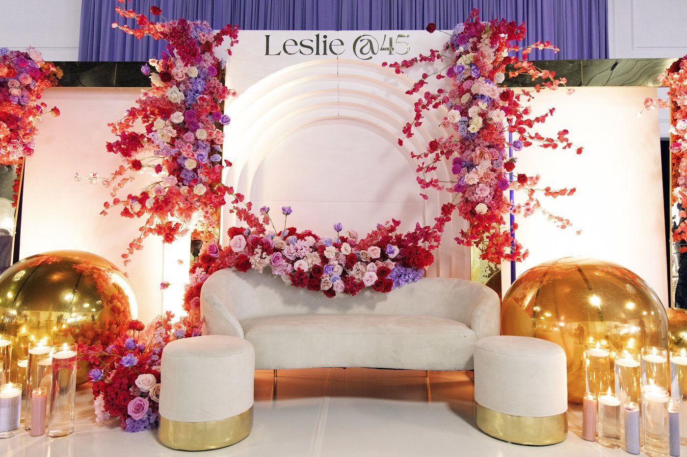 A white stage with a cherry blossom floral cascade, cream sofa and gold spheres set for a 45th birthday at The Hendrix