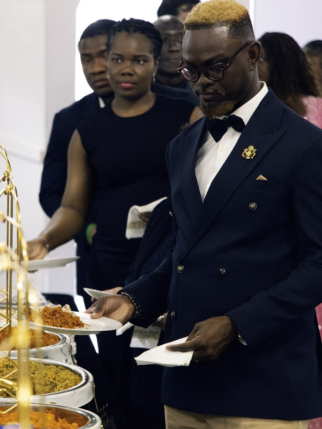 A guest in a navy tuxedo being served party rice from the buffet at a Nigerian celebration in The Hendrix, Stafford