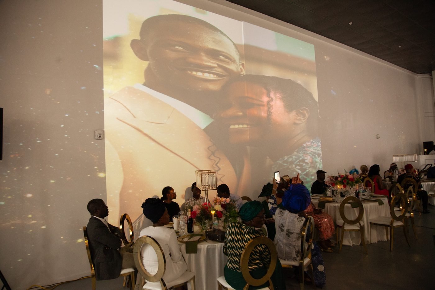 Wedding guests at round tables watching the couple's photographs play across the video wall in the Mansion at The Hendrix